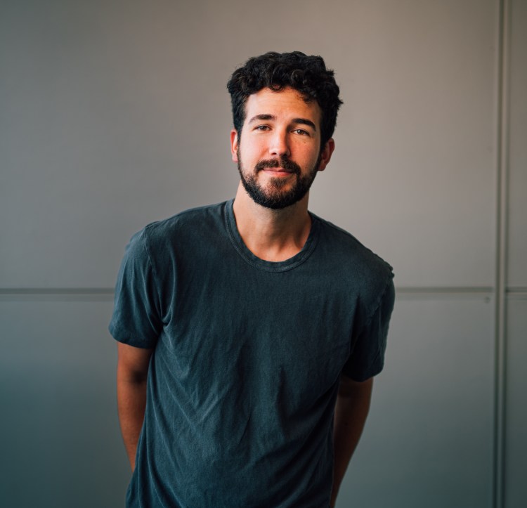 Photo of Ben Johnson in a gray t-shirt standing against a white wall