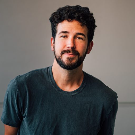 Photo of Ben Johnson in a gray t-shirt standing against a white wall